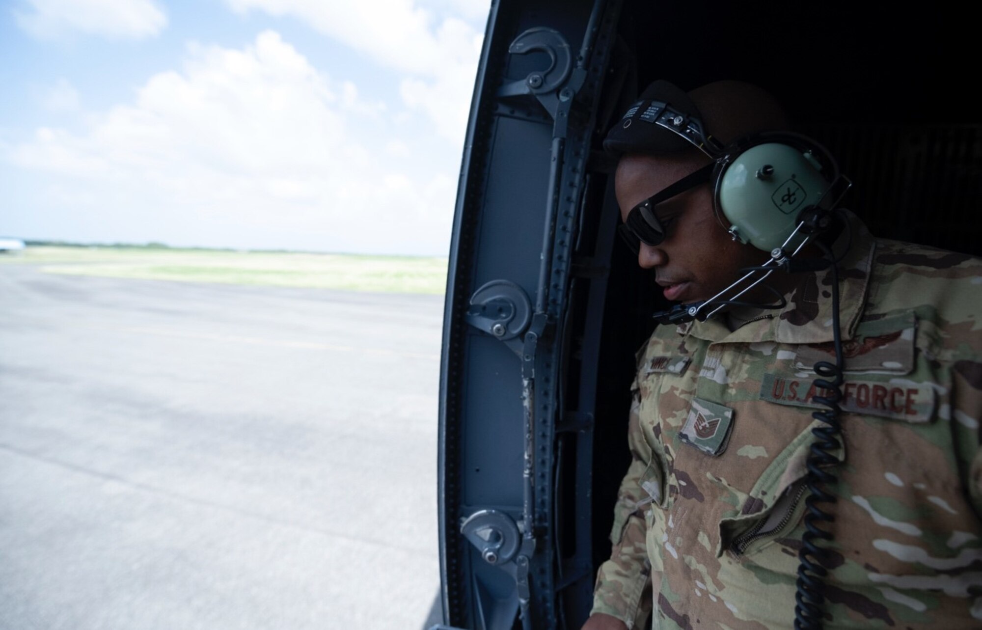 A uniformed Airman in sunglasses looks out an open compartment