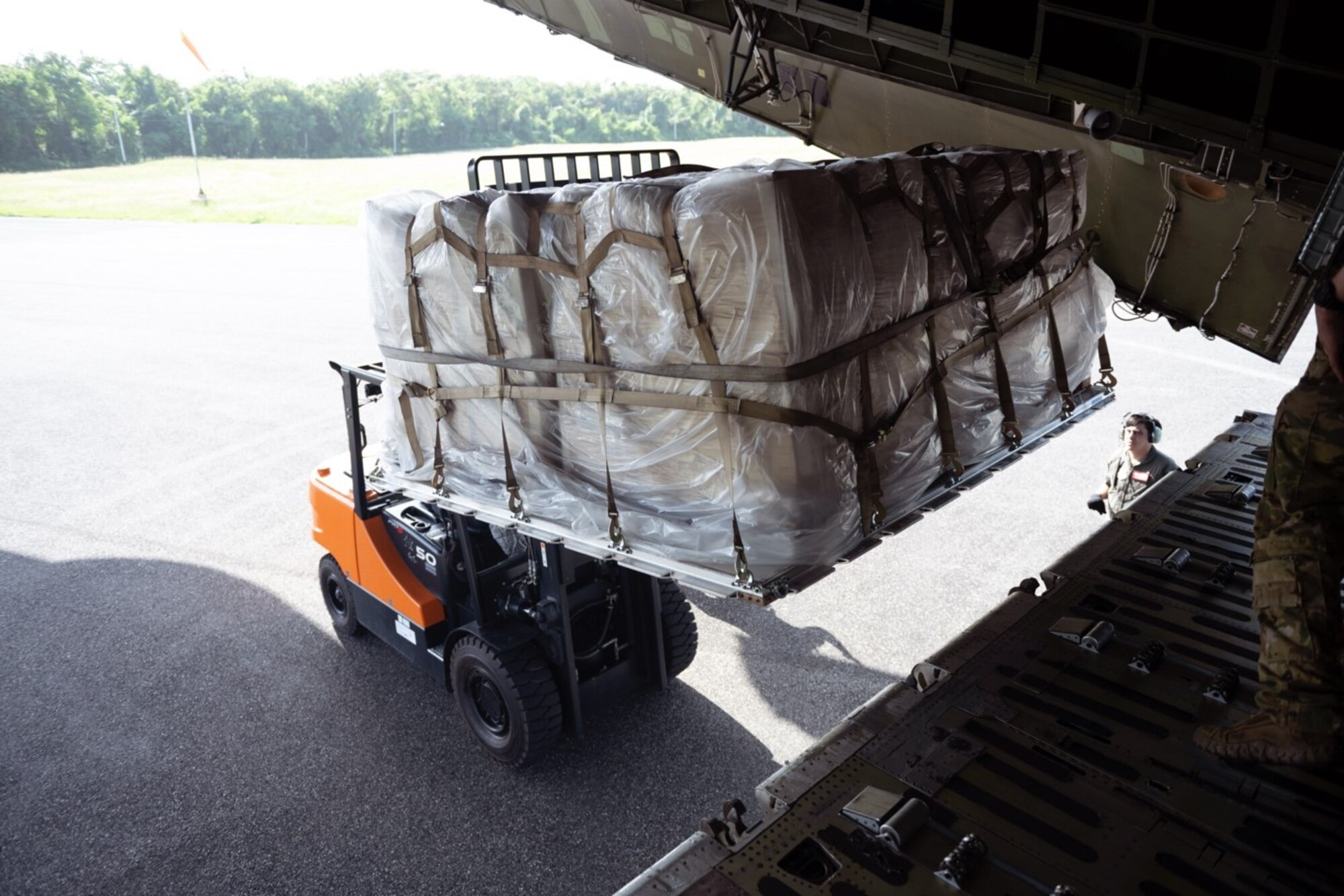 A pallet is loaded onto a k-loader off the back of a C-5 on a sunny day