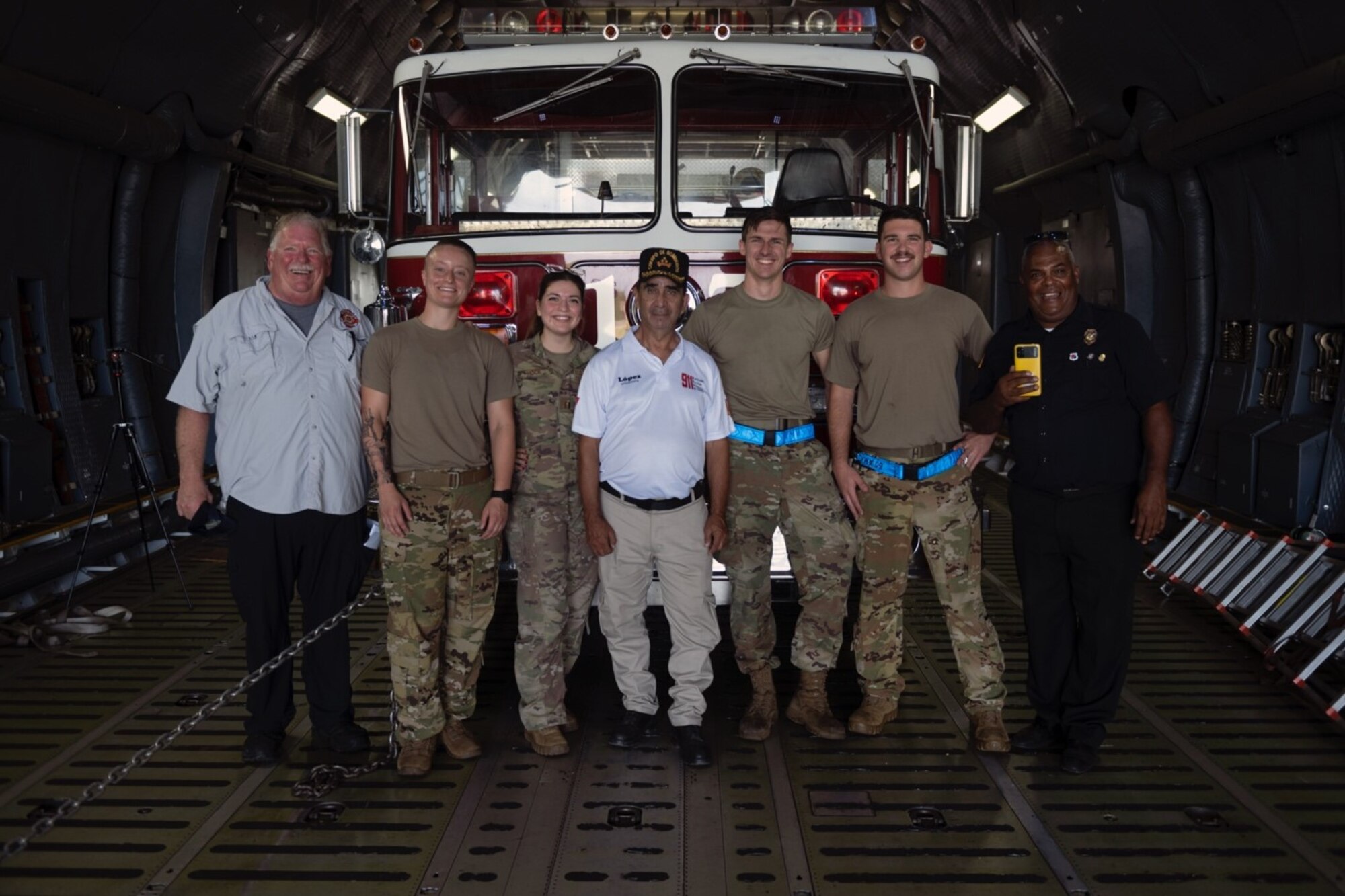 Uniformed Airmen and civilians stand in the cargo bay of a C-5 in front of pallets of humanitarian aid