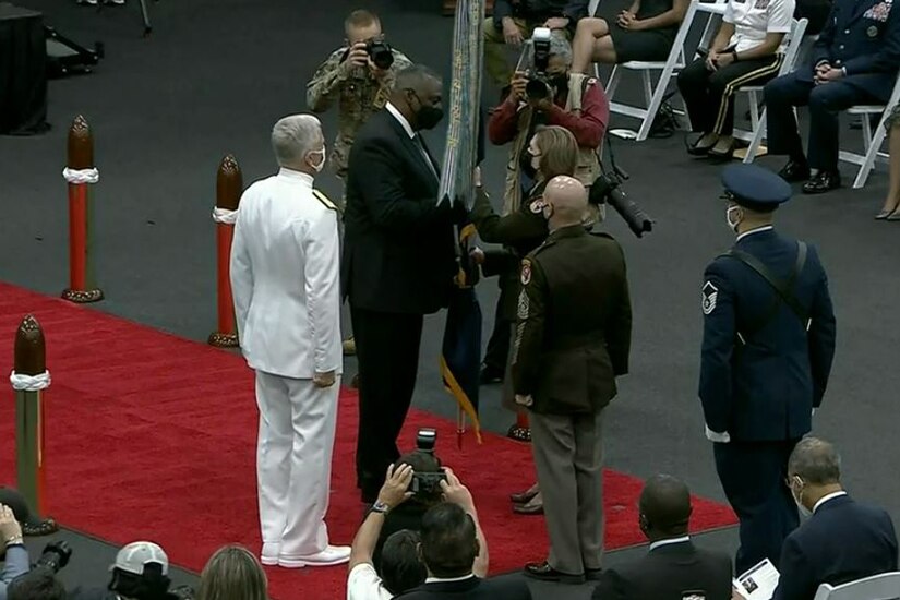 Secretary of Defense Lloyd J. Austin III  hands a large flag to a military officer.