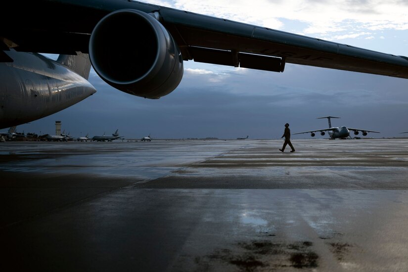 An airman walks on the flight line towards a C-5 on an overcast day