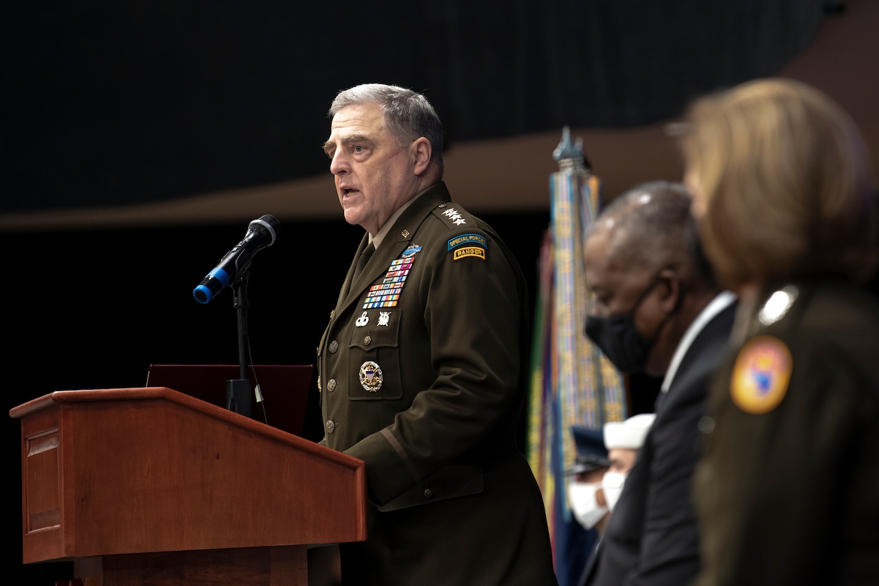 Aman in a military uniform stands at a lectern. There are two people in the foreground.