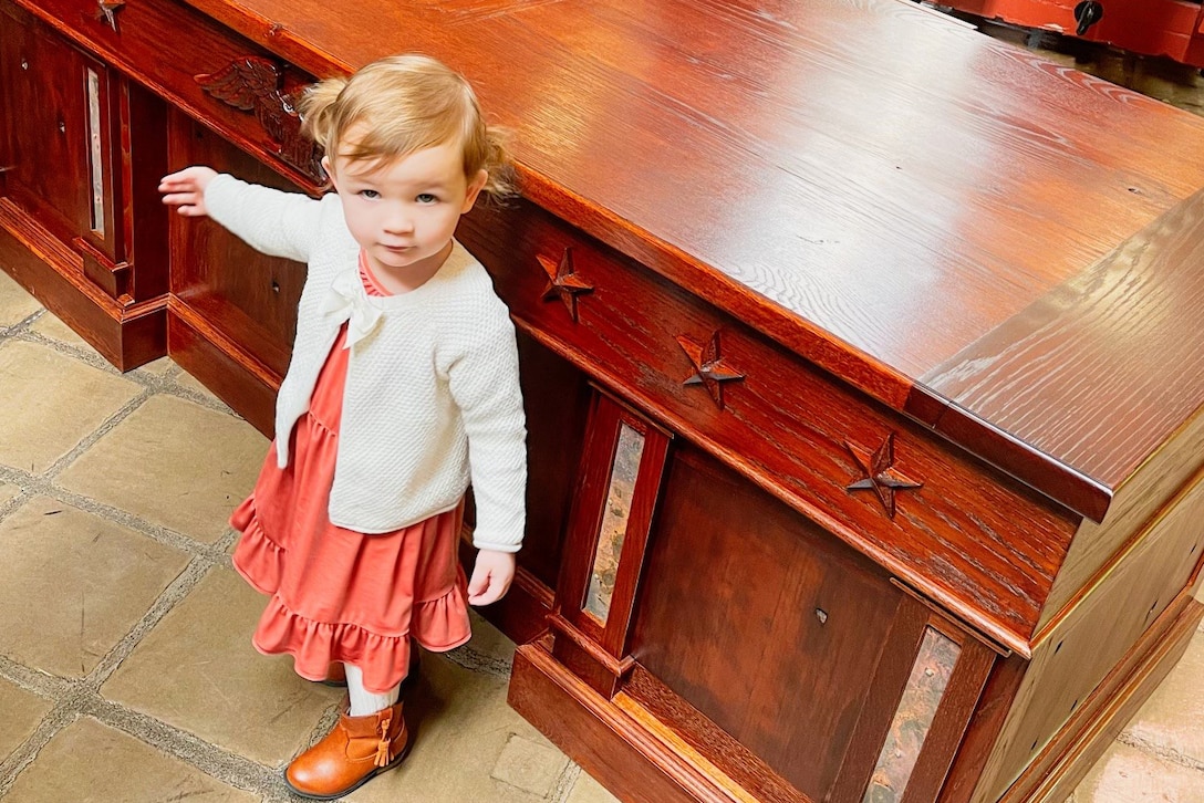 A little girl stands in front of a desk.