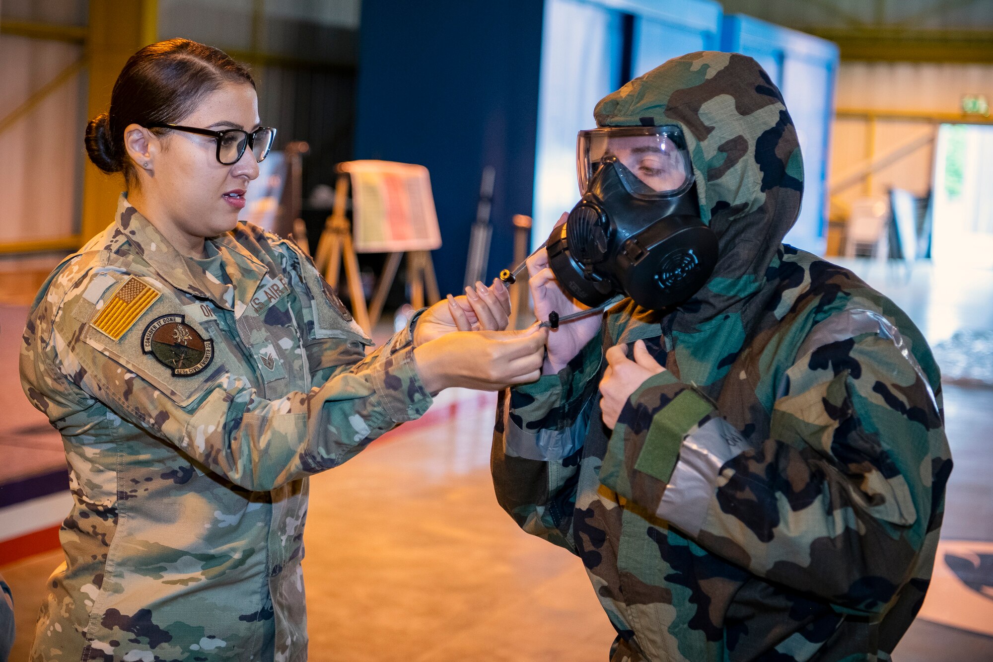 U.S. Air Force Staff Sgt. Ashley Ortiz, left,  423d Civil Engineer Squadron emergency management NCO in charge of plans and operations, assists Maj. Erica Balfour, 423d Communications Squadron commander, with her Mission Oriented Protective Posture gear during Ability to Survive and Operate training at RAF Alconbury, England, Aug. 27, 2021. Airmen from the 501st Combat Support Wing participated in the ATSO rodeo to get a refresher on how to properly utilize their MOPP gear in a potential chemical environment. (U.S. Air Force photo by Senior Airman Eugene Oliver)