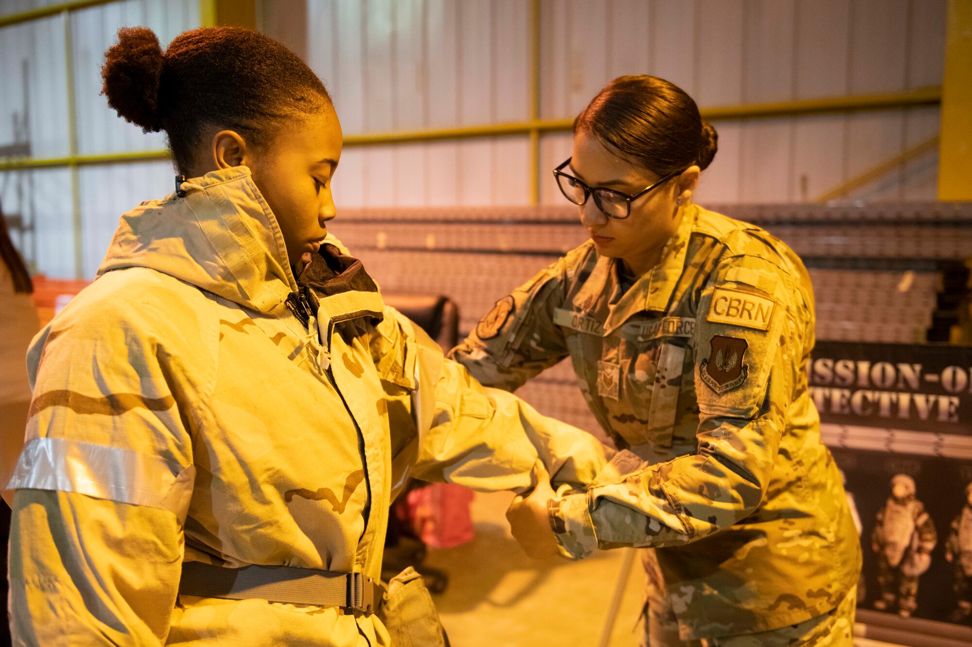 U.S. Air Force Staff Sgt. Ashley Ortiz, right,  423d Civil Engineer Squadron emergency management NCO in charge of plans and operations, assists a 501st Combat Support Wing member with their Mission Oriented Protective Posture gear during Ability to Survive and Operate training at RAF Alconbury, England, Aug. 26, 2021. Airmen participated in the ATSO rodeo to get a refresher on how to properly utilize their MOPP gear in a potential chemical environment. (U.S. Air Force photo by Senior Airman Jennifer Zima)
