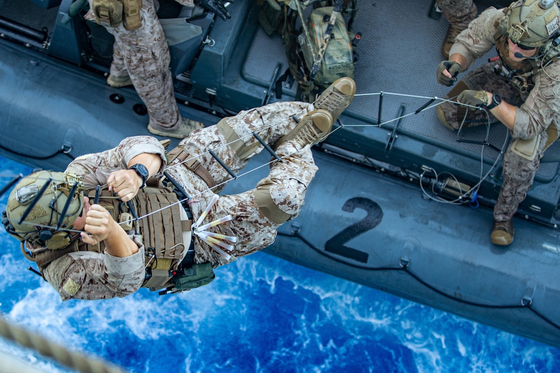 A Marine climbs a caving ladder from a rubber raft in the ocean.