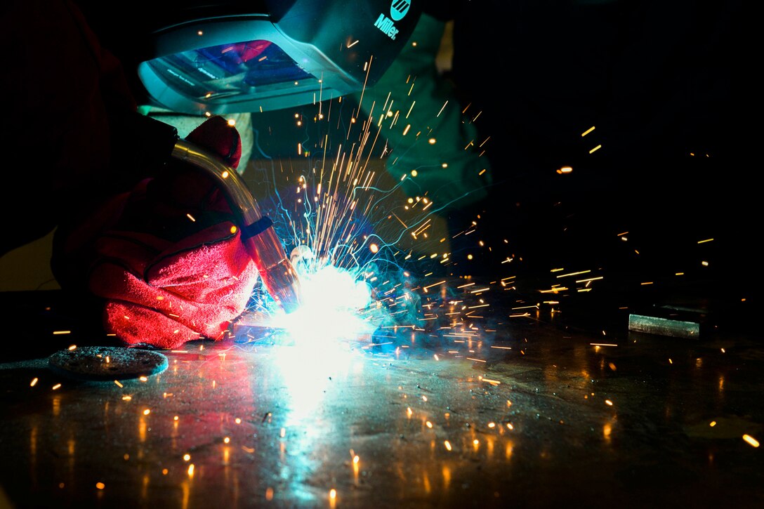 An airman welds two pieces of metal together as sparks fly.