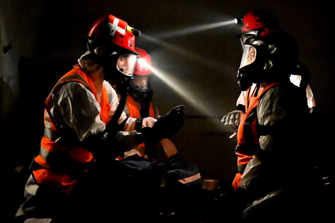 Airmen wearing protective gear talk in a dark area.