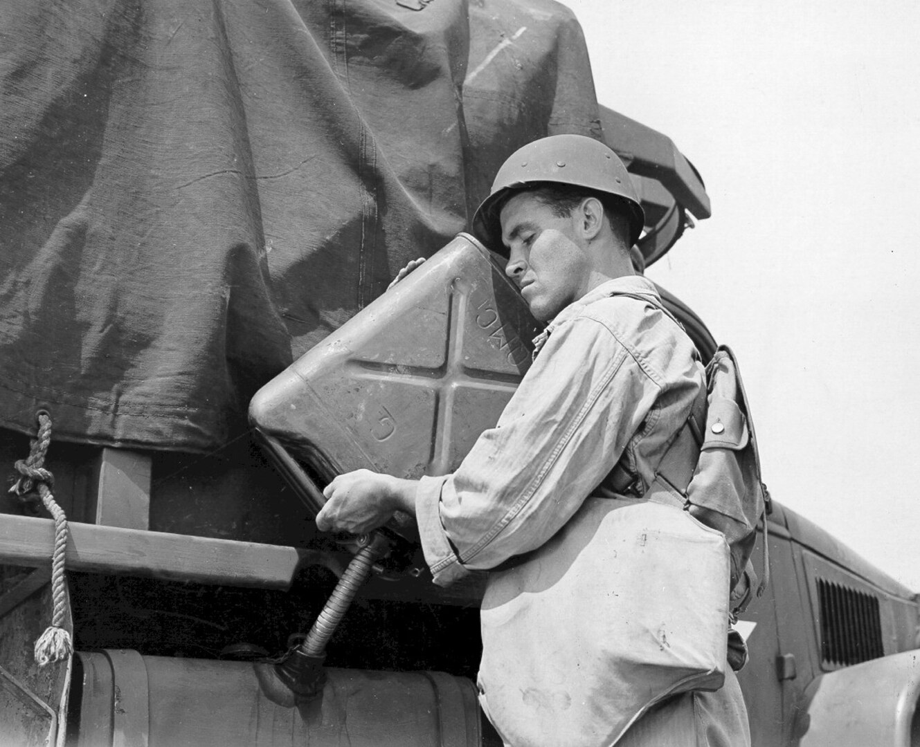 a WWII GI fills a fuel tank with a gas can