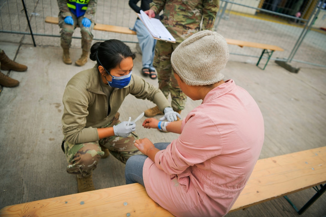 A service member kneels and touches the arm of a seated civilian.