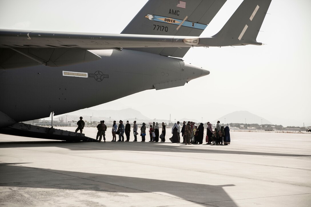 Civilians stand in line by a rear ramp onto an open aircraft.