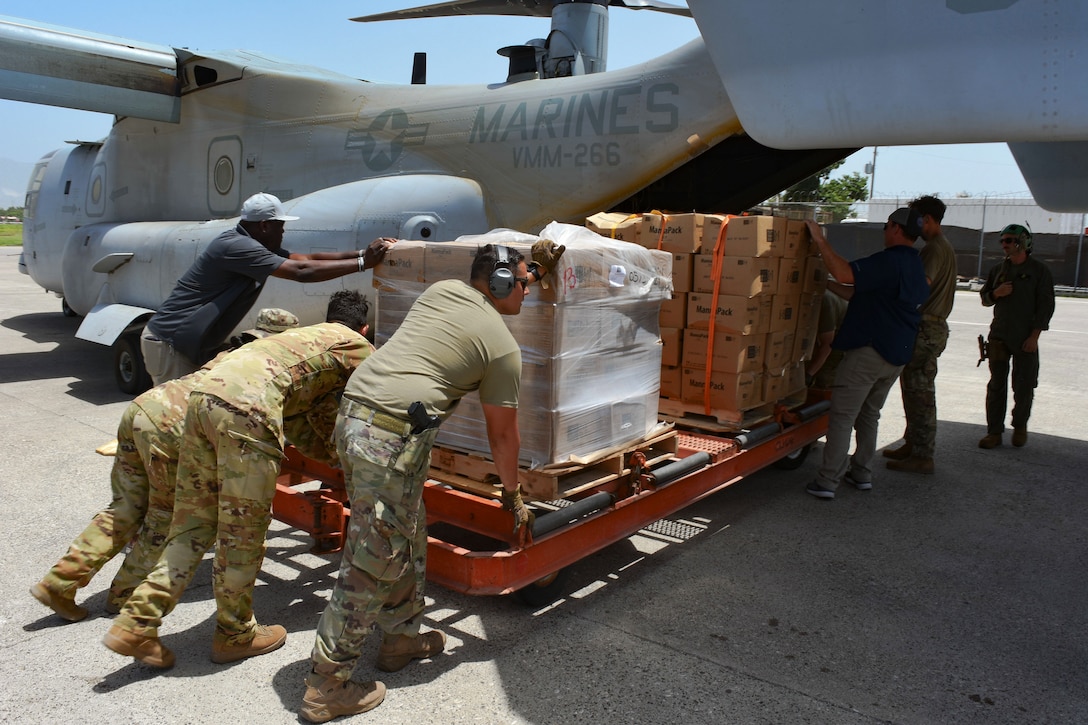Service members and civilian push pallets of boxes toward the back of an open aircraft.