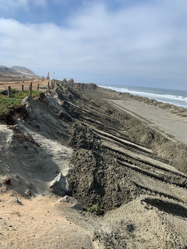 Mounds of sand on a beach with construction equipment.