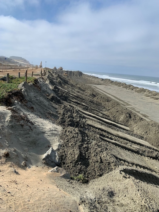 Mounds of sand on a beach with construction equipment.