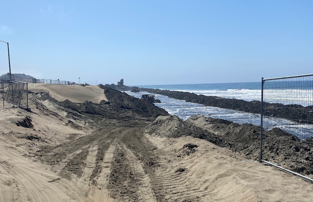 Mounds of sand on a beach with construction equipment.