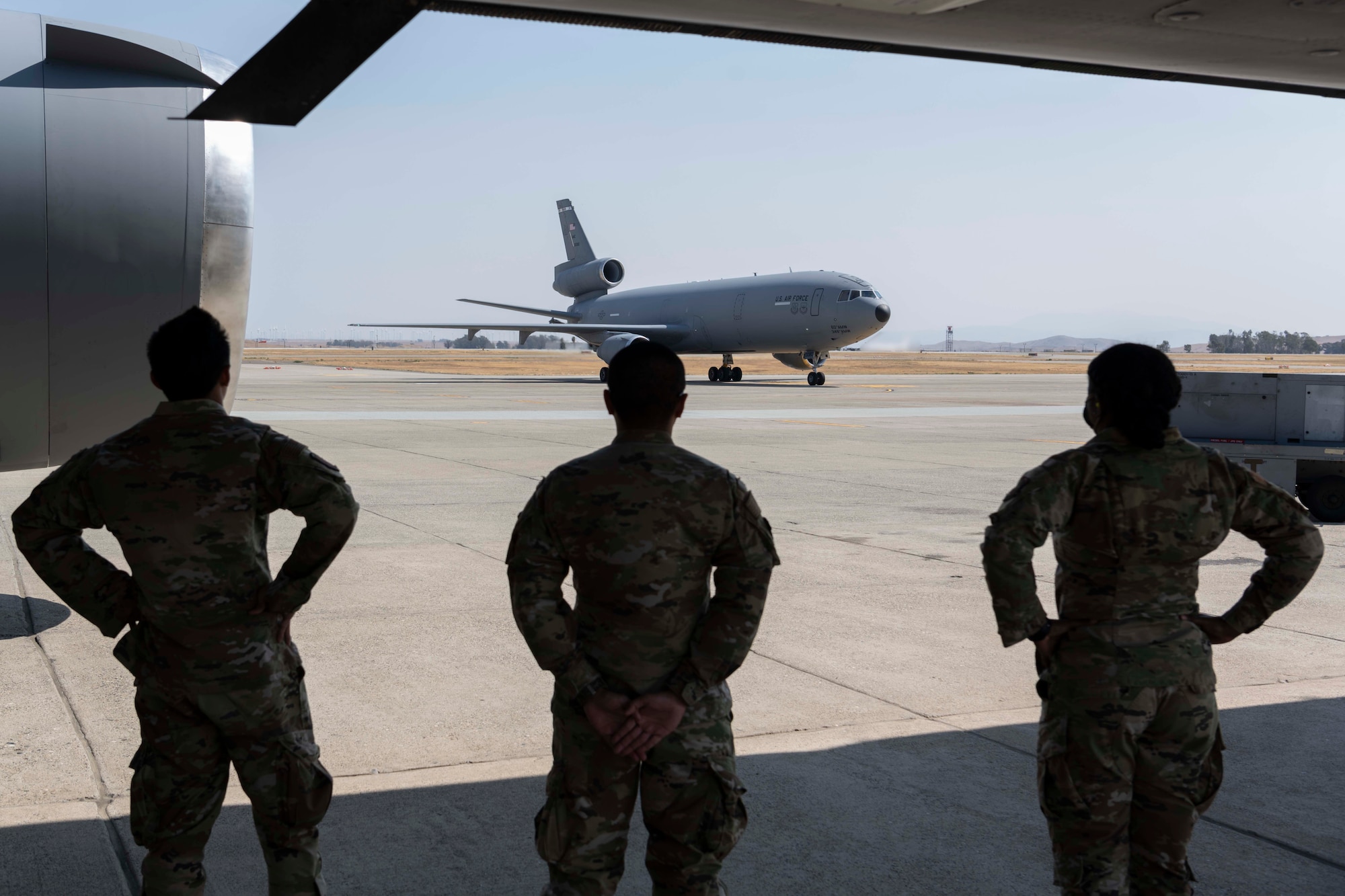 Three Airmen watch a plane taxi on the flight line