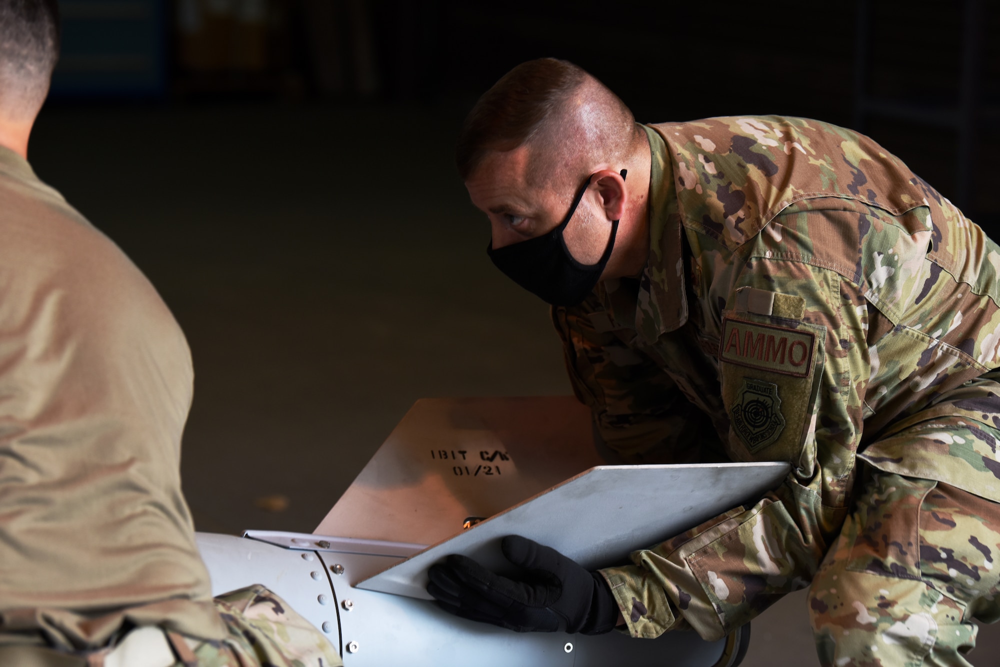 People in a camo uniform work around large cylindrical munitions