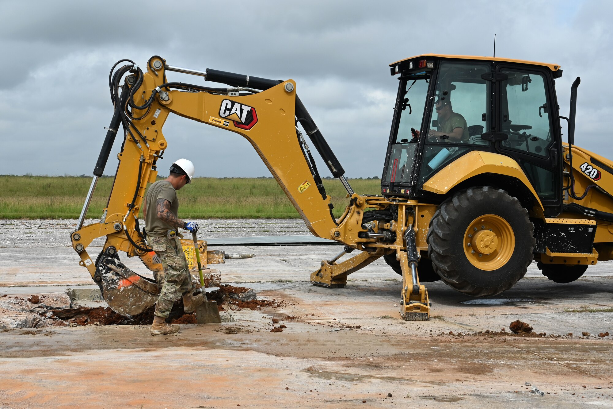 U.S. Air Force Tech. Sgt. Patrick Moyer (white hard hat) and Staff Sgt. Alexander Henderson (backhoe), both from the 169th Civil Engineer Squadron, South Carolina Air National Guard, excavate part of the runway during an Expedient and Expeditionary Airfield Damage Repair (E-ADR) demonstration at McEntire Joint National Guard Base, South Carolina, Aug. 27, 2021. The purpose of the training is to provide just enough, just in time repair capability with minimal cost and materials in a wartime situation. (U.S. Air National Guard photo by Senior Master Sgt. Edward Snyder, 169th Fighter Wing Public Affairs)