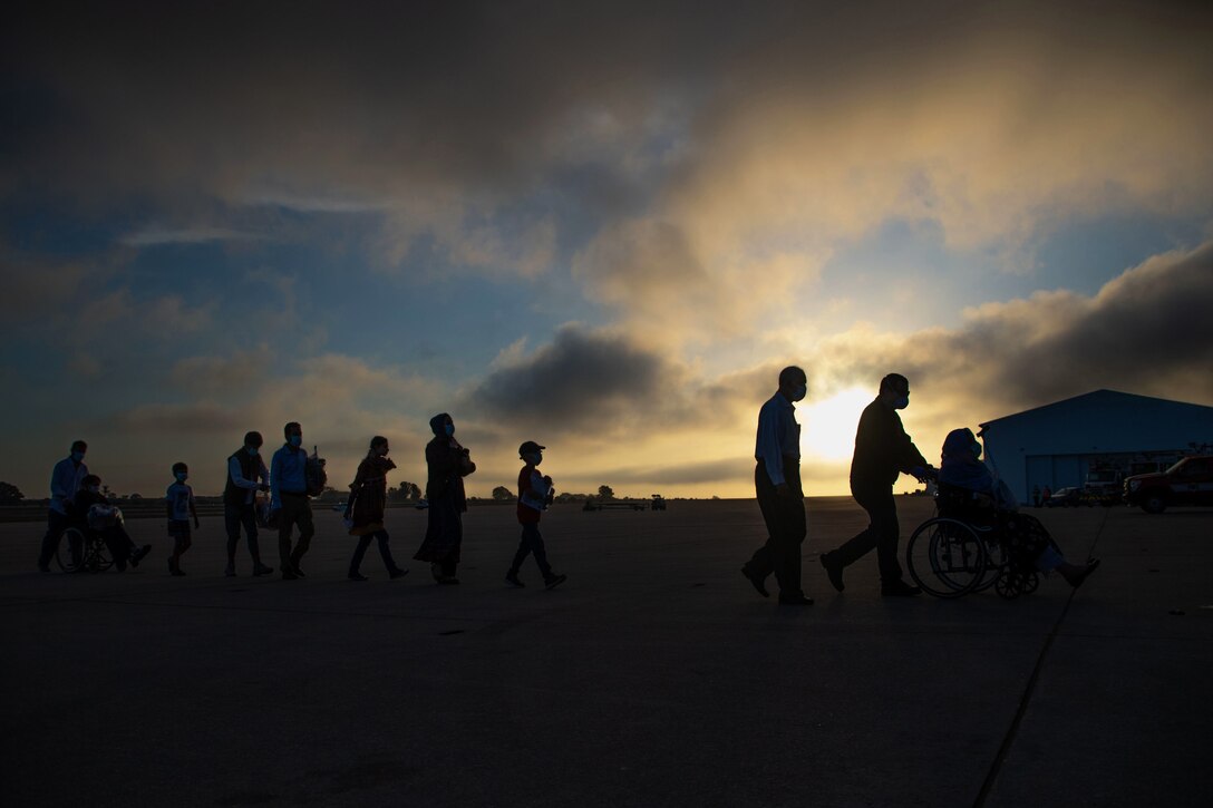 People shown in silhouette walk across a flightline.