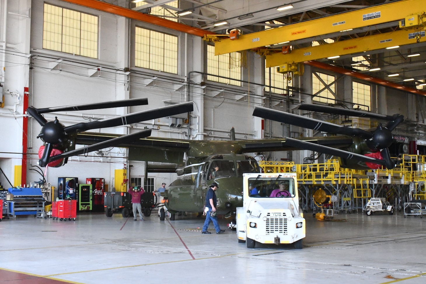 A tug tows a V-22 aircraft out of a hangar.