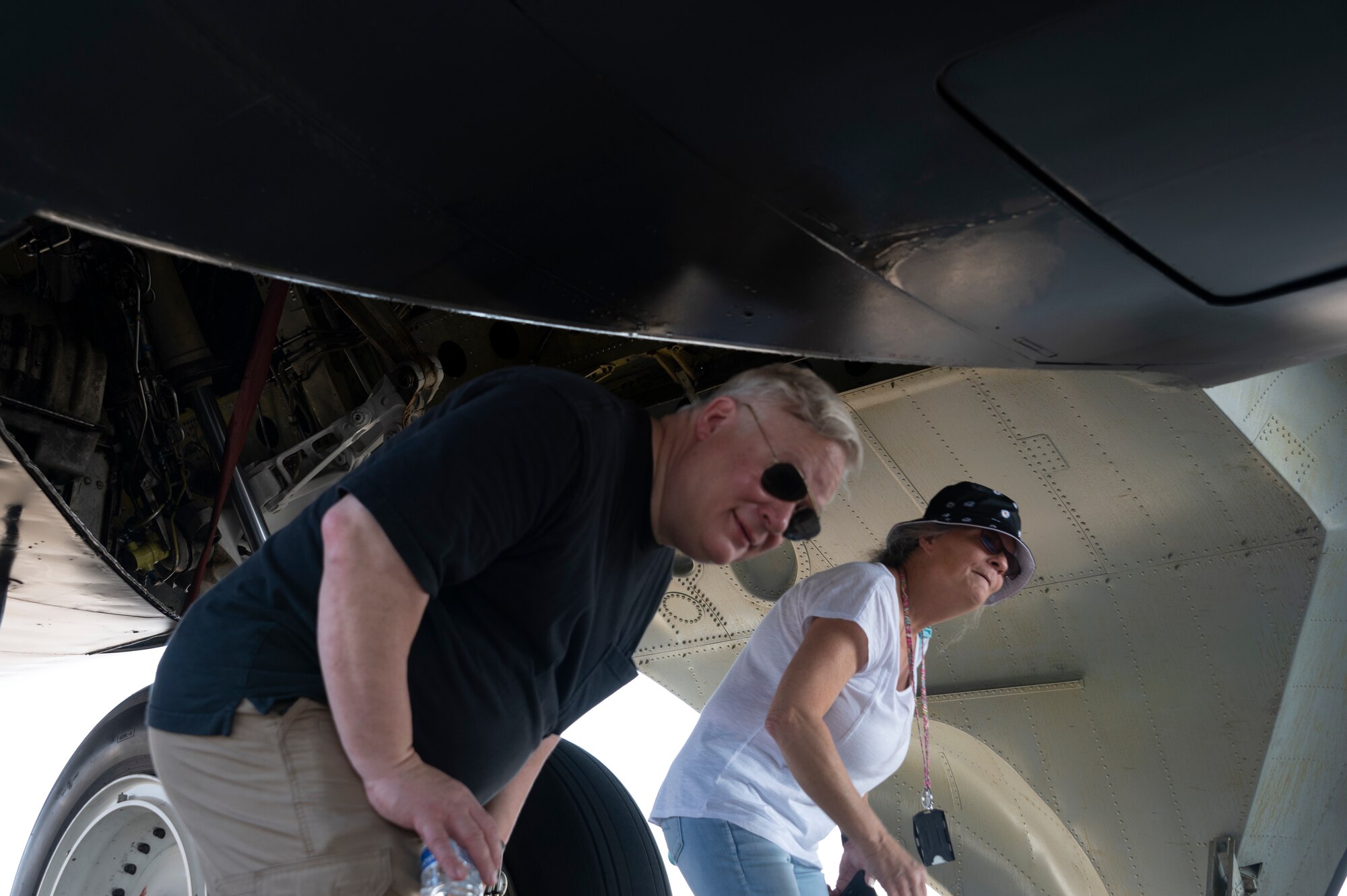Two people walk underneath an airplane.