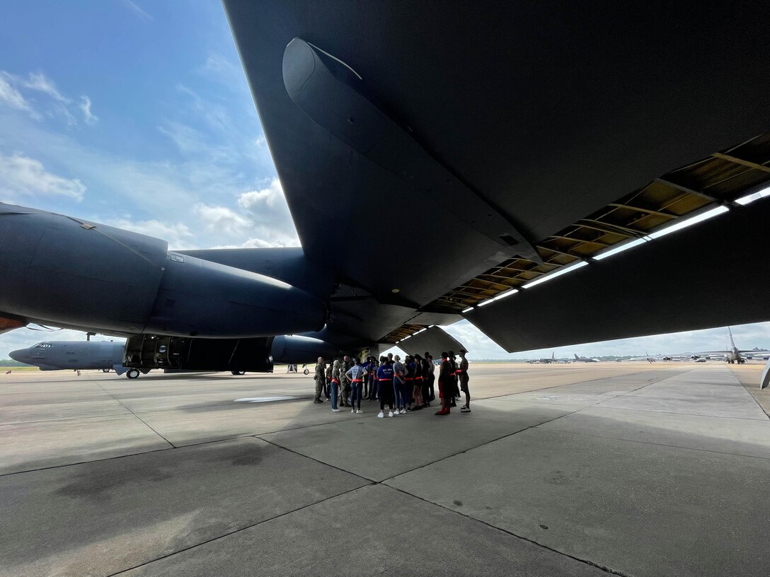 A group of people stand underneath the wing of an airplane.