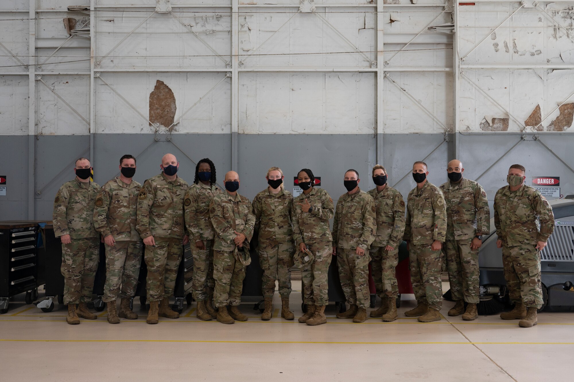Twelve people stand in front of a gray wall.