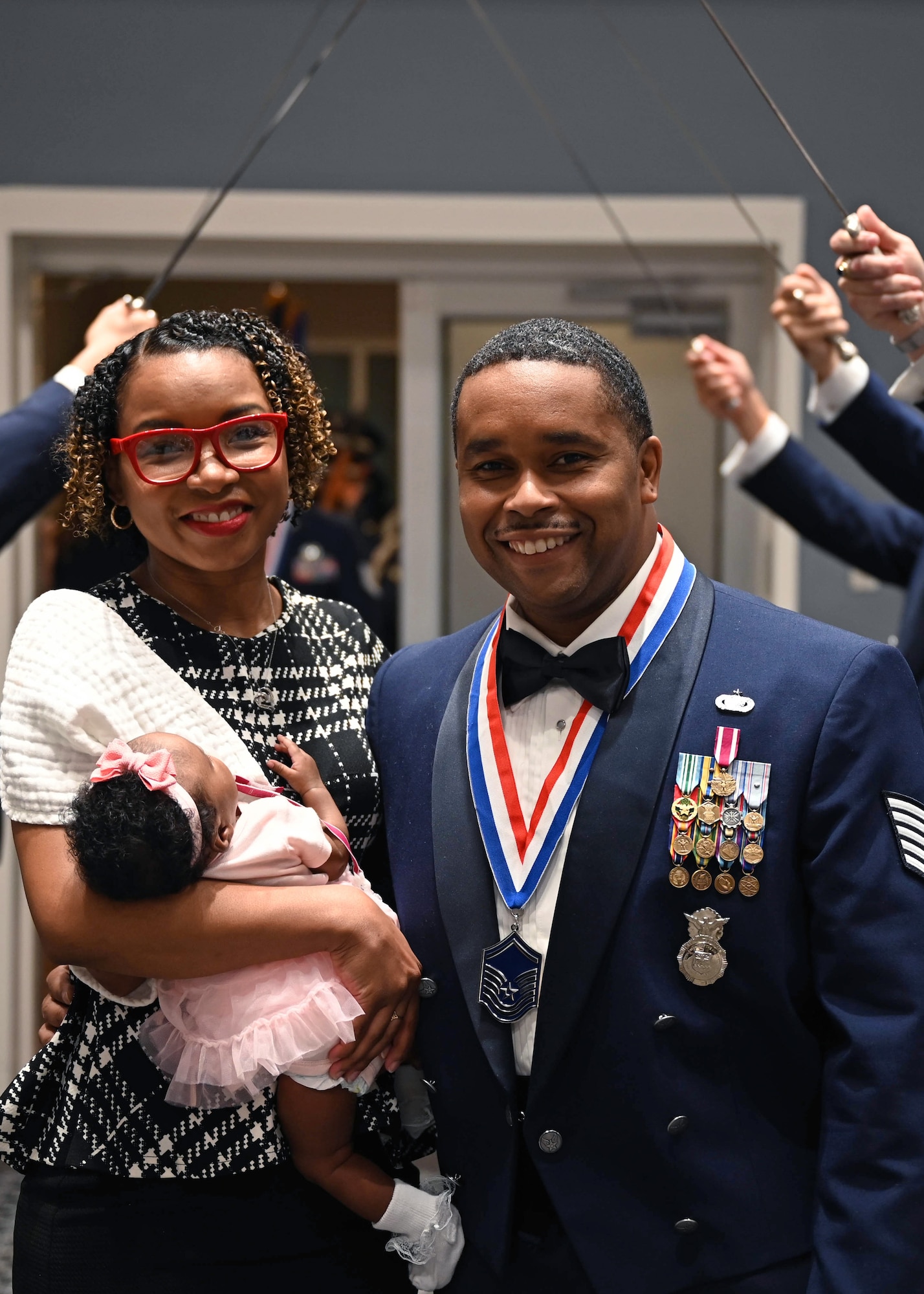 Master Sgt. select Shaun Segrow poses with his family for a photo in front of a saber cordon.