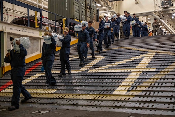 Sailors walk food and water down to a landing craft, utility (LCU), in Arlington’s well deck prior to delivering humanitarian aid to the Port of J�r�mie, Haiti, Aug. 31, 2021.