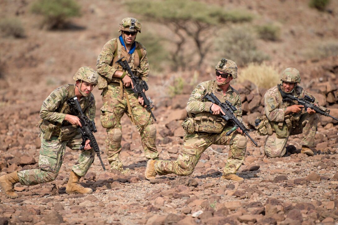 Four service members move through desert terrain.