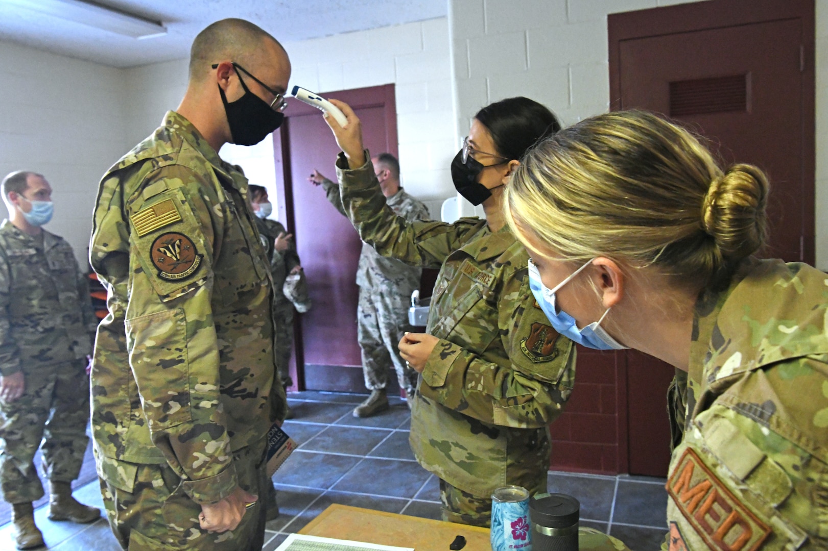 Oregon National Guard Tech. Sgt. Meghan Olson, 173rd Medical Group, checks the temperature of Senior Master Sgt. John Wyman, 270th Air Traffic Control Squadron, while Capt. Jaimie Nealy reviews his paperwork during an inprocessing briefing for Airmen activated to support hospitals across Oregon Sept. 2, 2021, at Kingsley Field in Klamath Falls, Oregon.