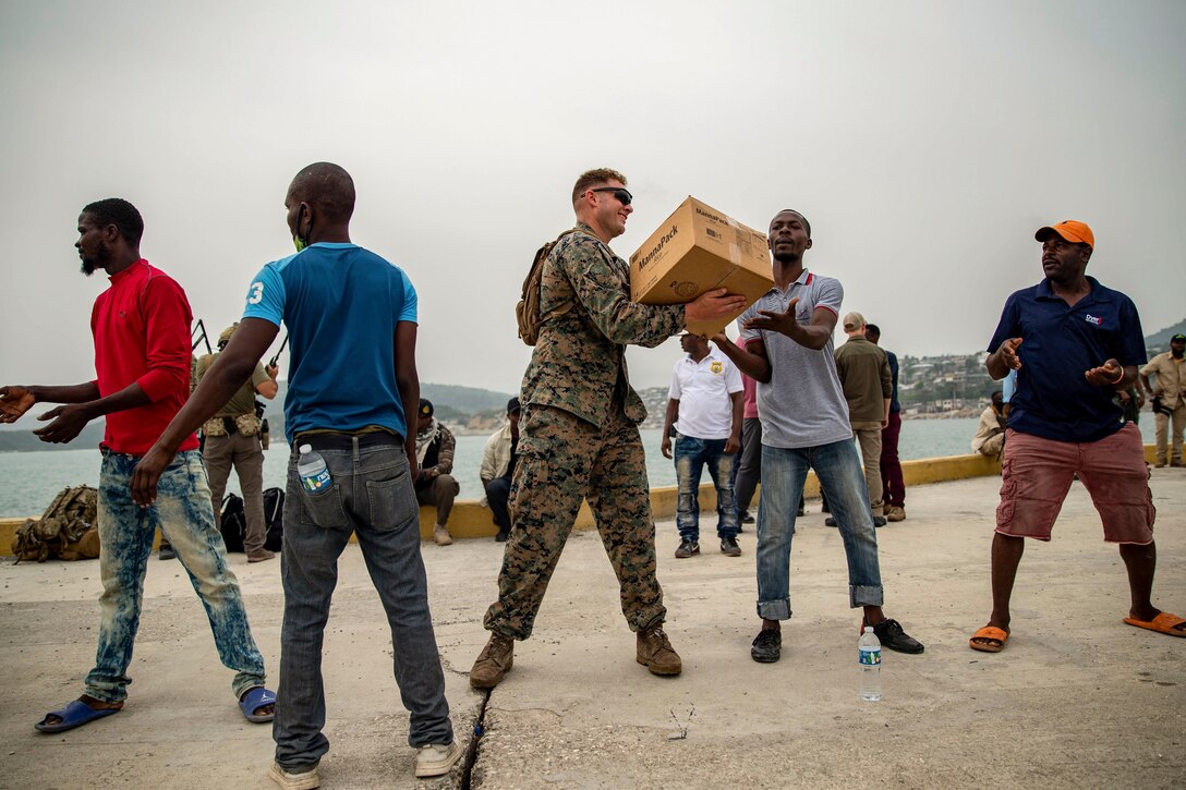 A Marine passes a box to a civilian as other civilians stand by to help.