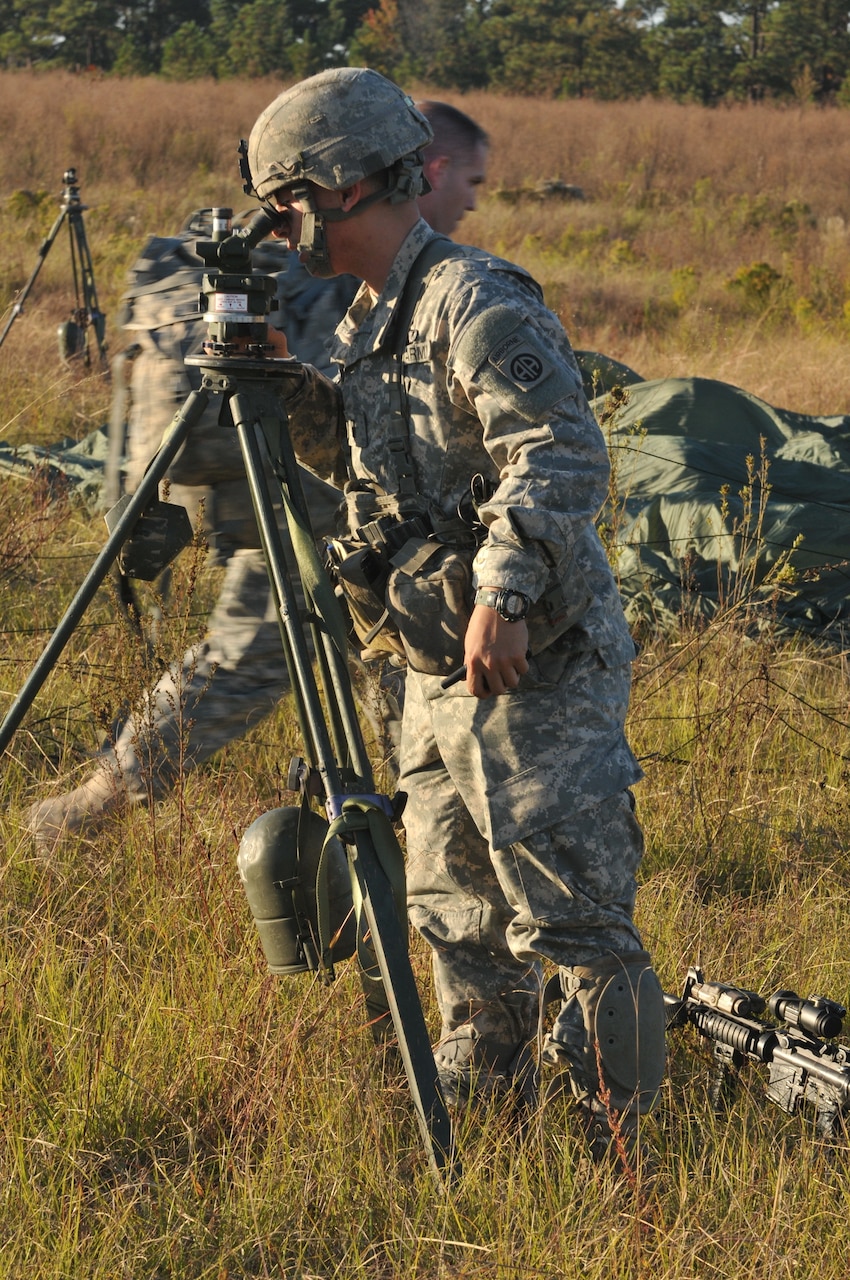 A soldier uses a device that sits on top of a tripod.
