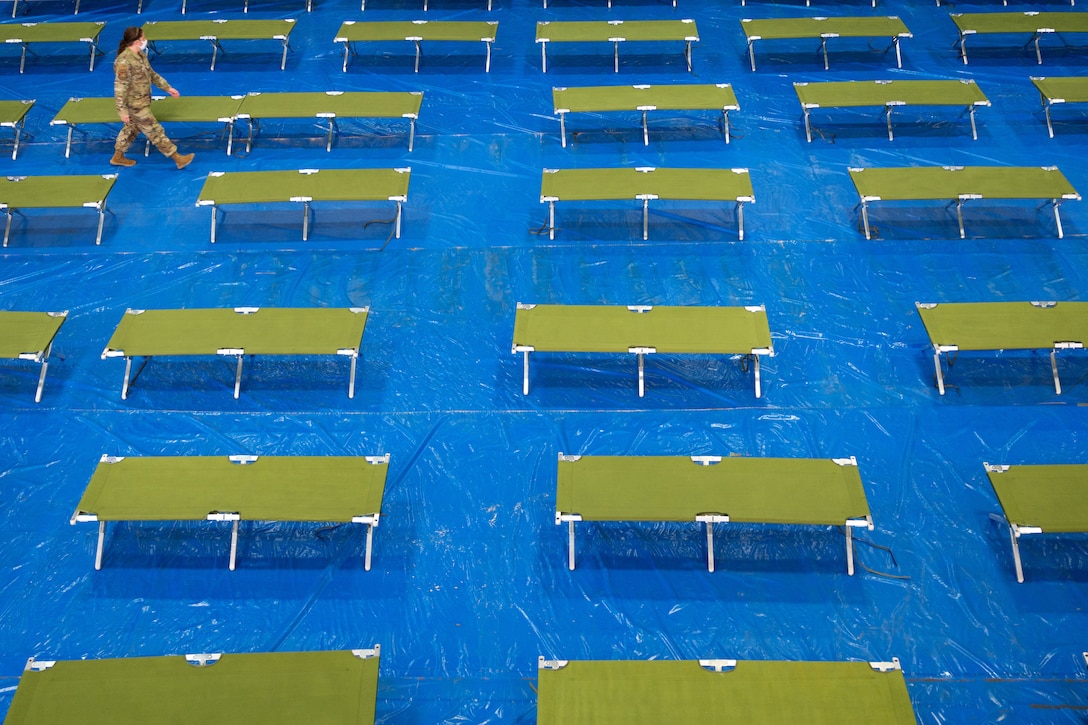 An airman walks through a large room full of temporary cots.
