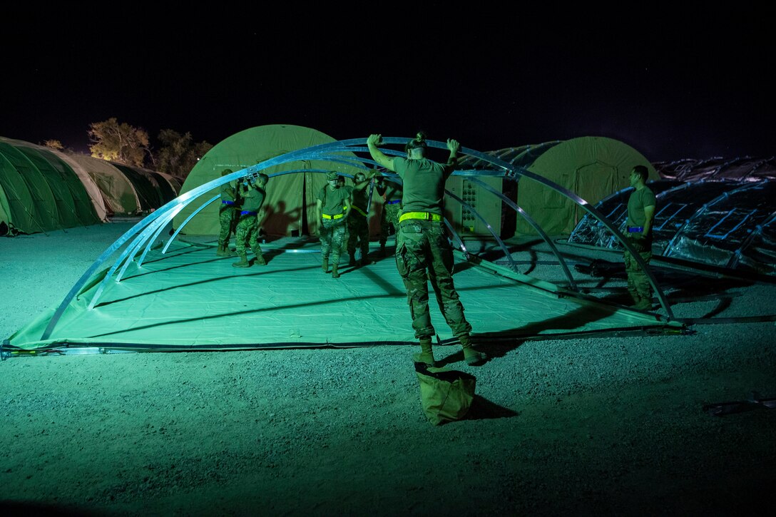 An airman sets up a large tent at night.