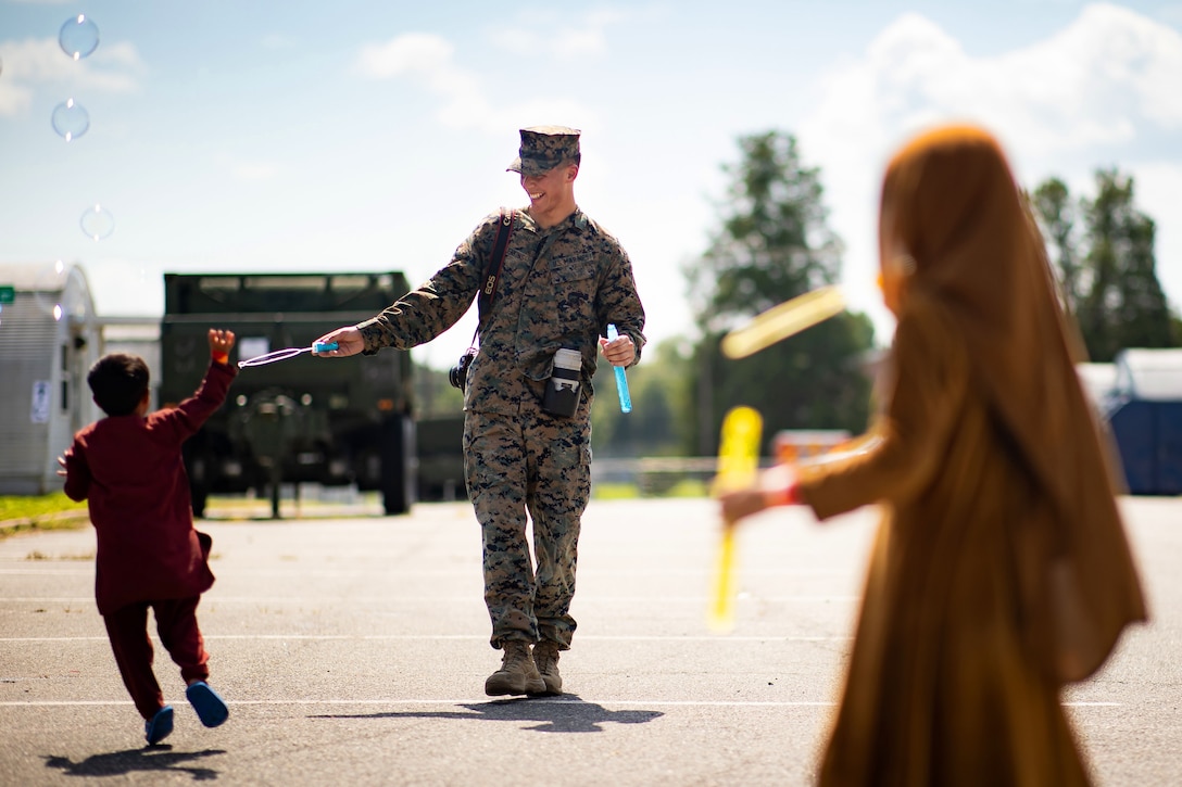 A Marine uses a wand to create bubbles, as a child reaches his hand skyward.