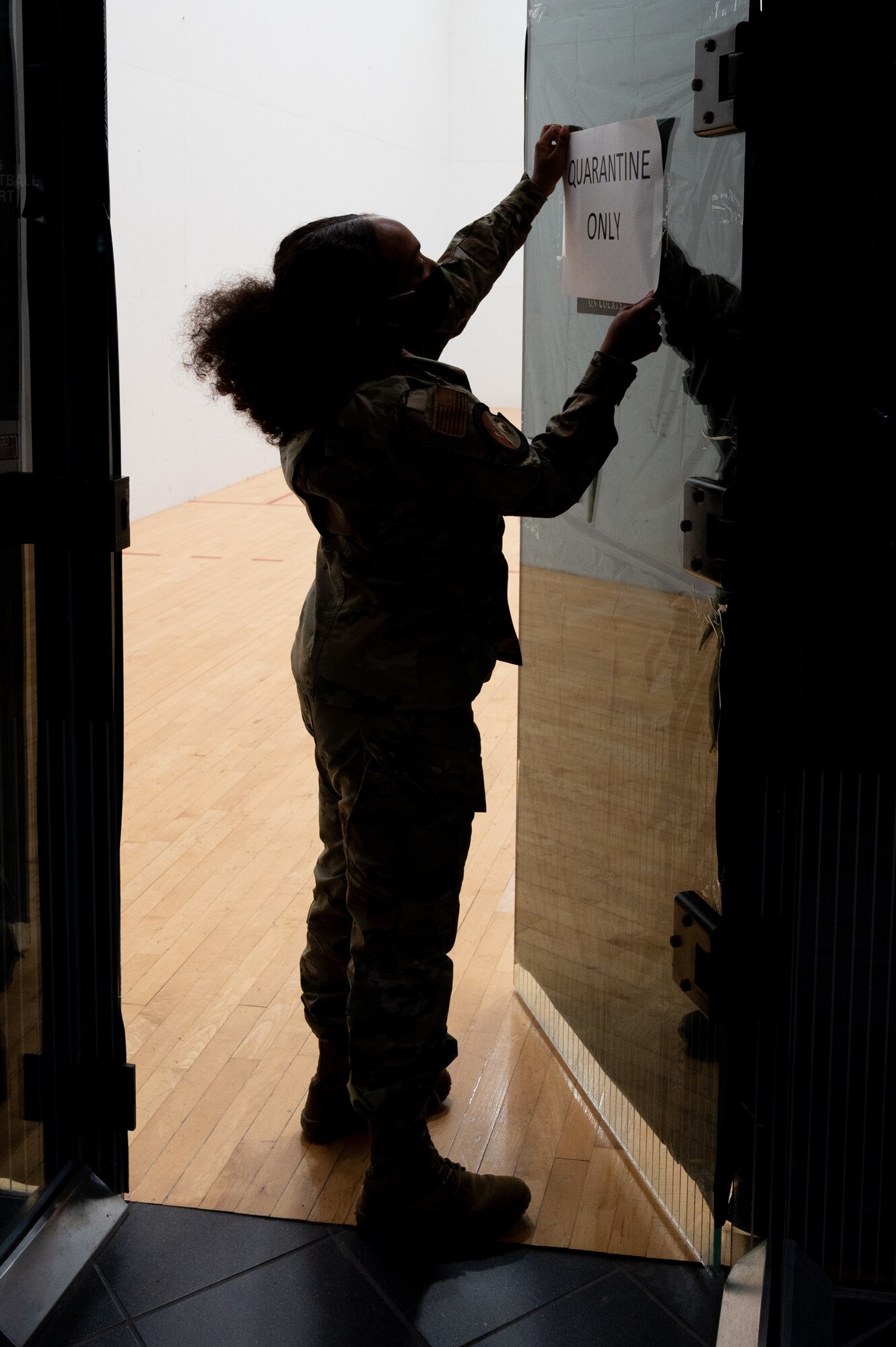 Senior Airman Kaela Prude, 49th Force Support Squadron fitness specialist, hangs a sign for COVID-19 mitigation efforts during Task Force-Holloman preparations Aug. 27, 2021 on Holloman Air Force Base, New Mexico. The Department of Defense, through U.S. Northern Command, and in support of the Department of Homeland Security, is providing transportation, temporary housing, medical screening, and general support for up to 50,000 Afghan evacuees at suitable facilities, in permanent or temporary structures, as quickly as possible. This initiative provides Afghan personnel essential support at secure locations outside Afghanistan.(U.S. Air Force photo by Tech. Sgt. BreeAnn Sachs)