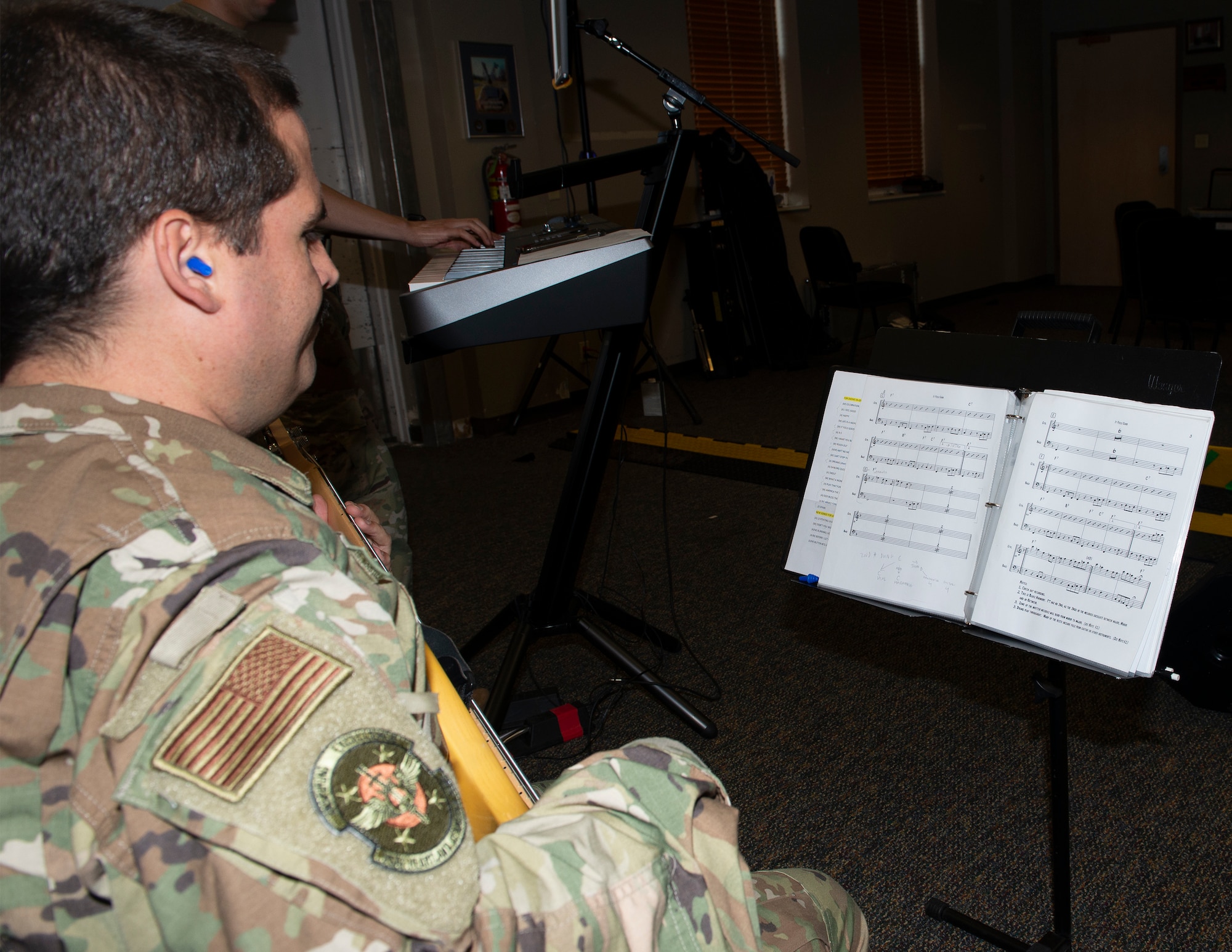 airmen in uniform sitting holding bass guitar with sheet music on a stand