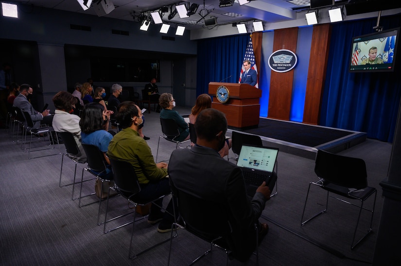person at lectern in briefing room with seated reporters