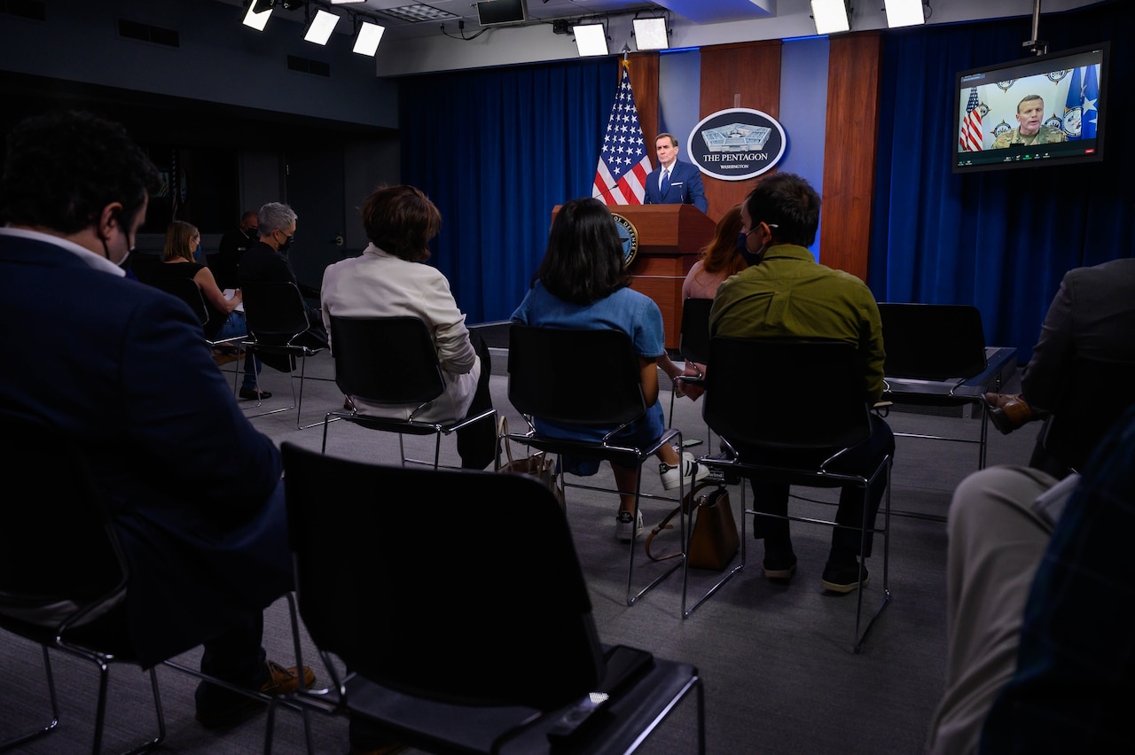 person at lectern in briefing room with seated reporters