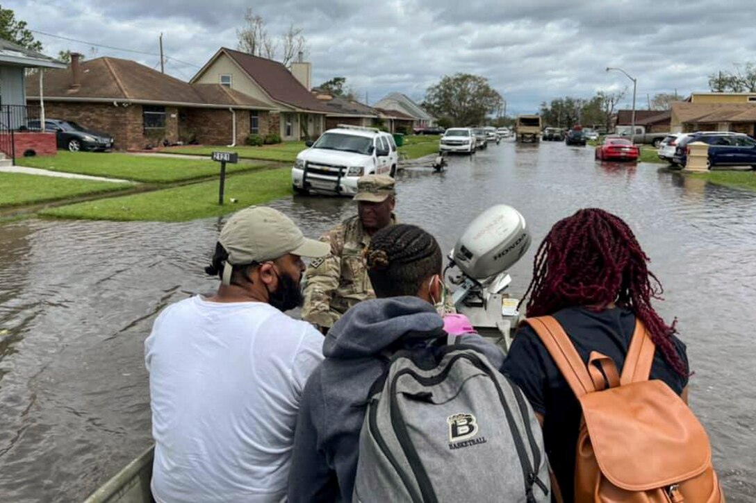 A National Guardsman steers a small boat with three civilians in it down a flooded street.