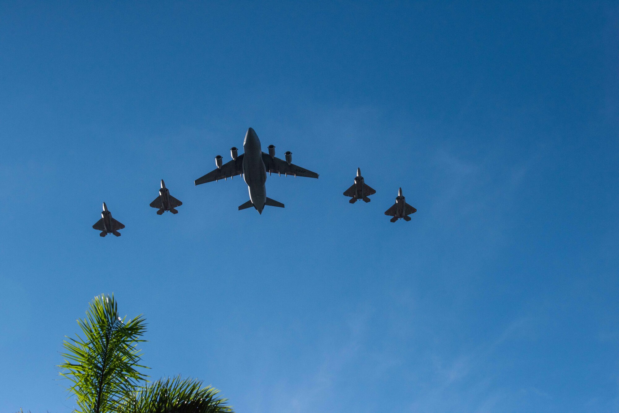 Photo of Four Hawaii F-22 Raptors and a C-17 Globemaster III from the 535th Airlift Squadron conducting a flyover.