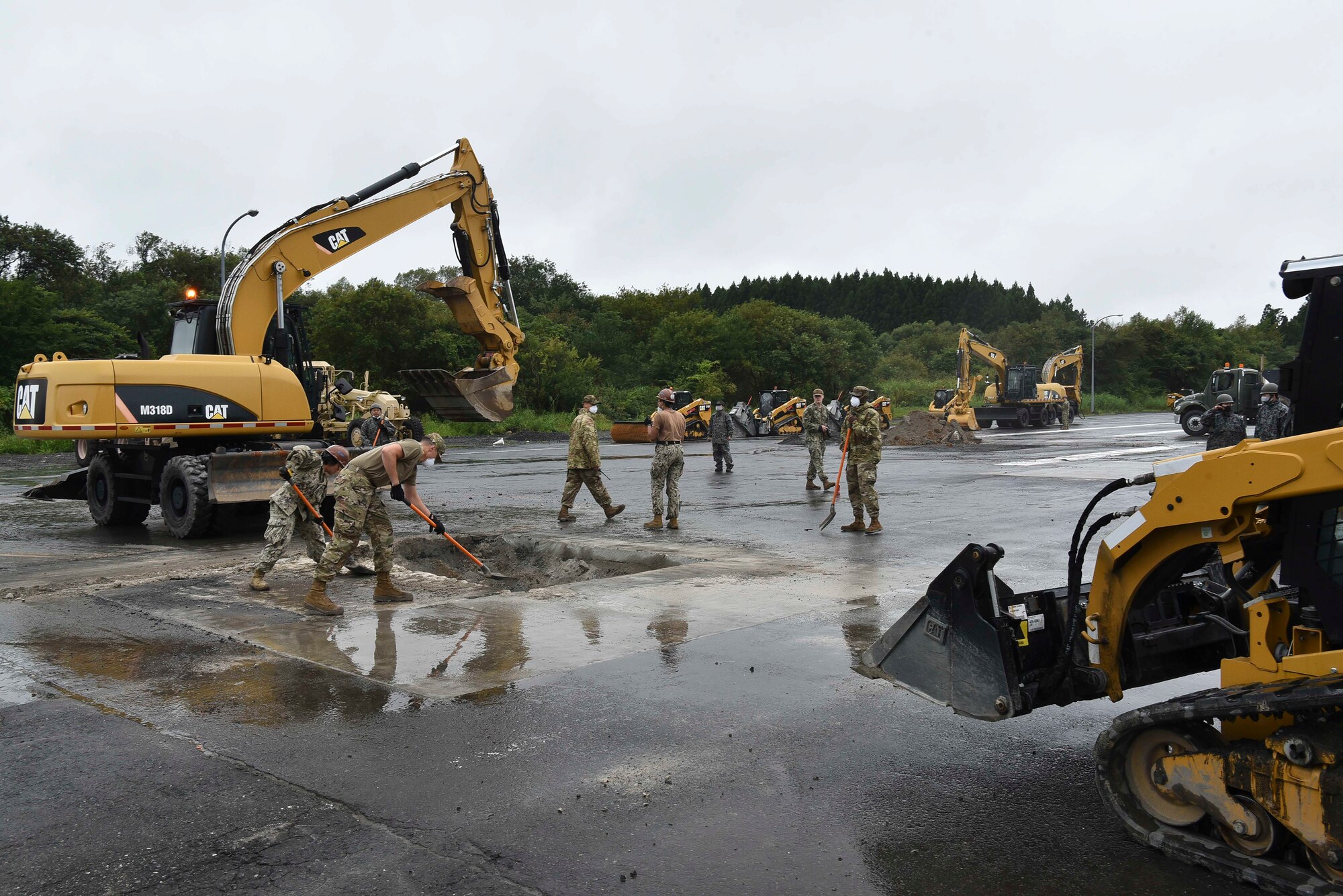 In a rapid airfield damage repair site two military members scrape rumble into a hole.