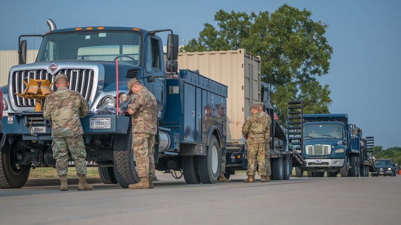 Troops gather by vehicles in a line.