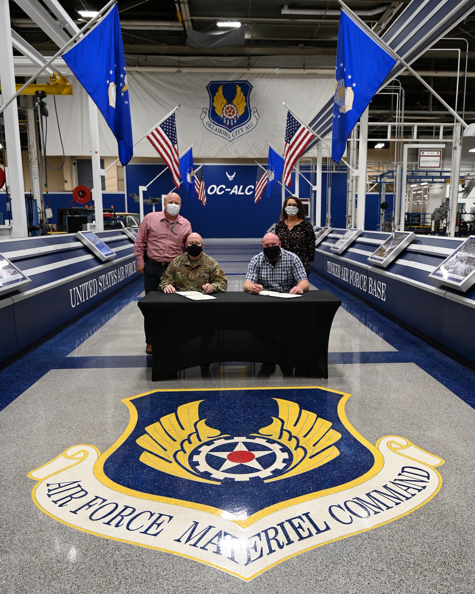 Two people standing, two people sitting at a table