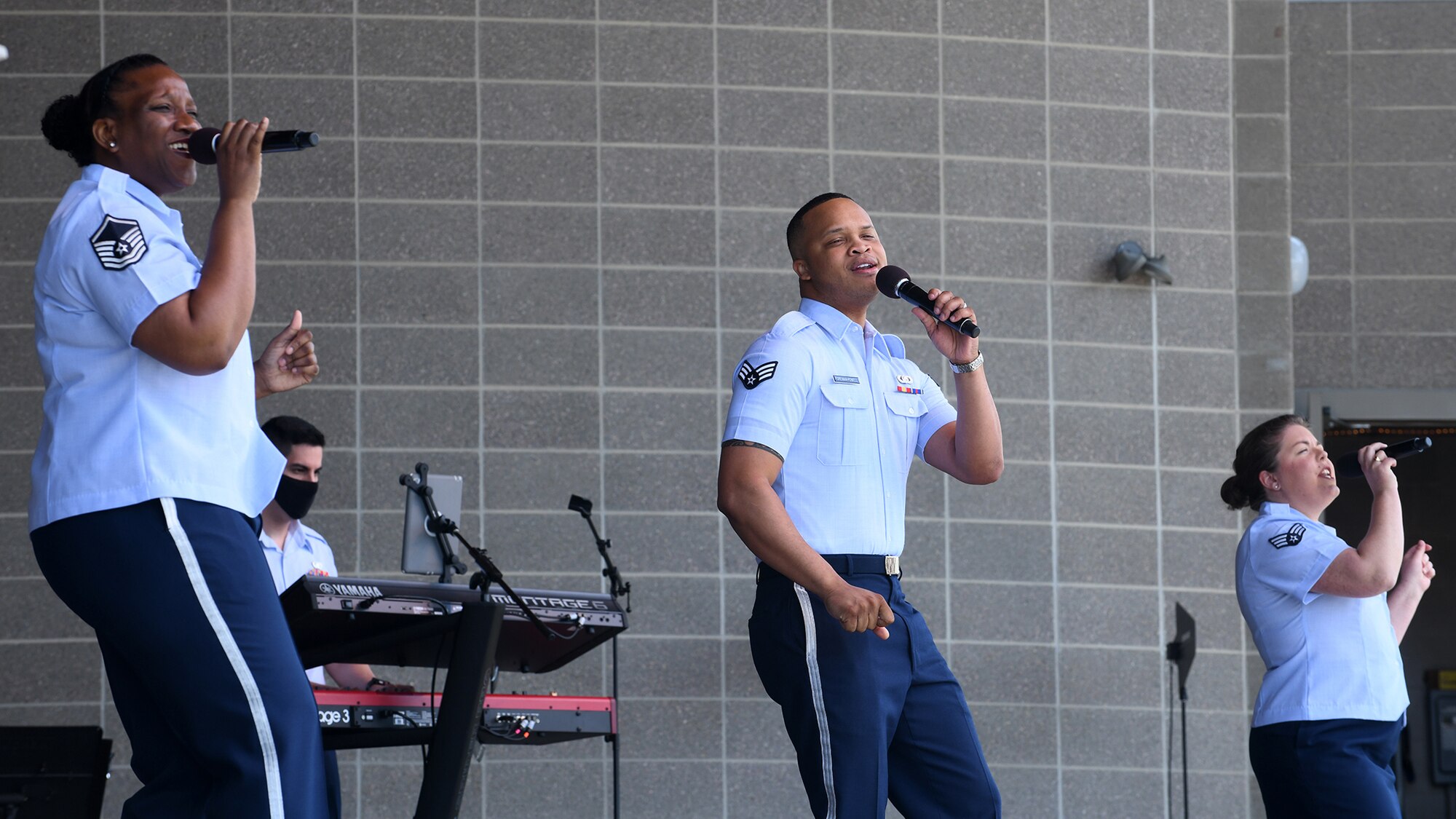three airmen in uniform holding microphones and singing