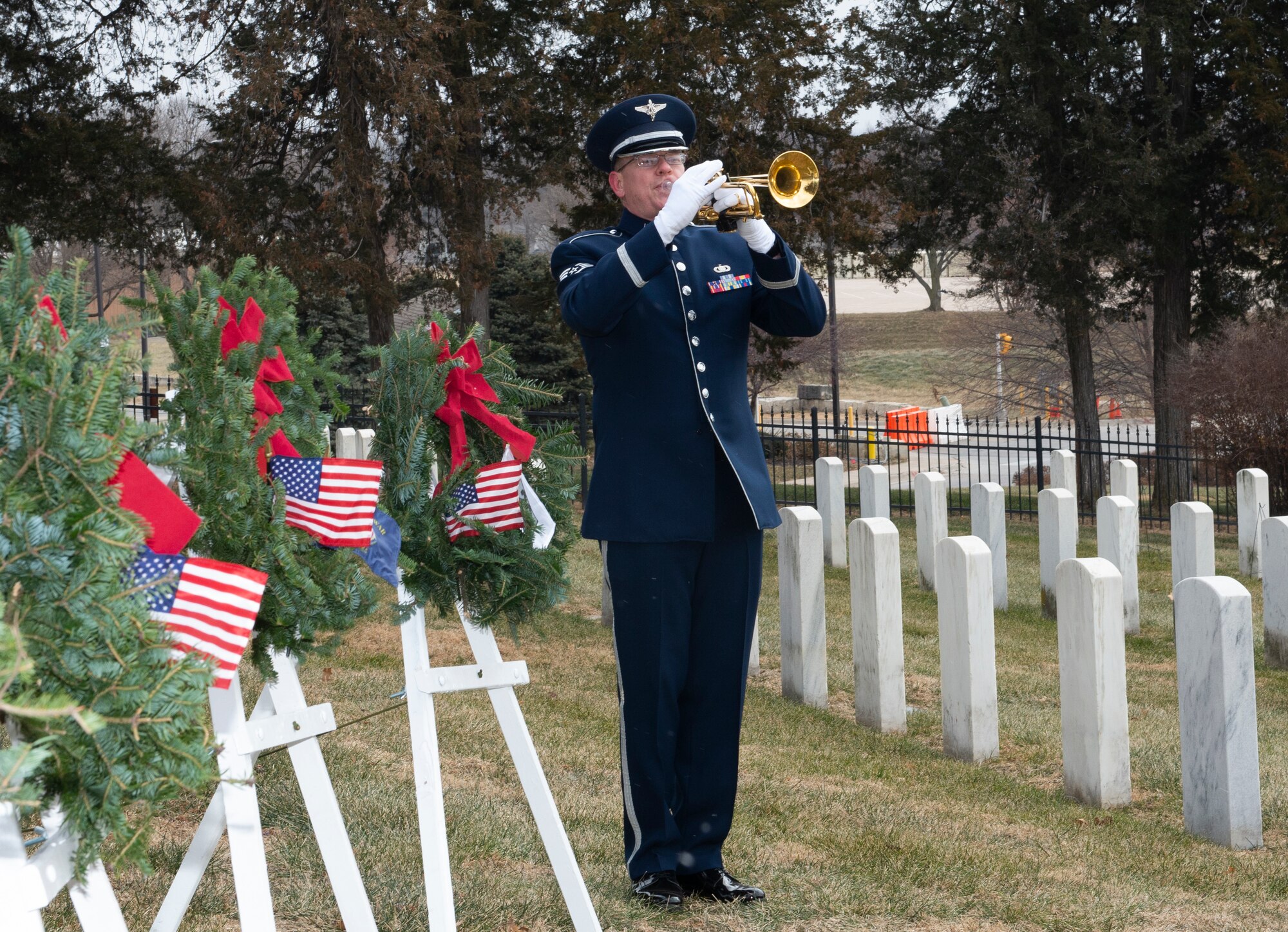 airmen in uniform standing in the middle of wreaths on easels and the first row of headstones at a cemetery