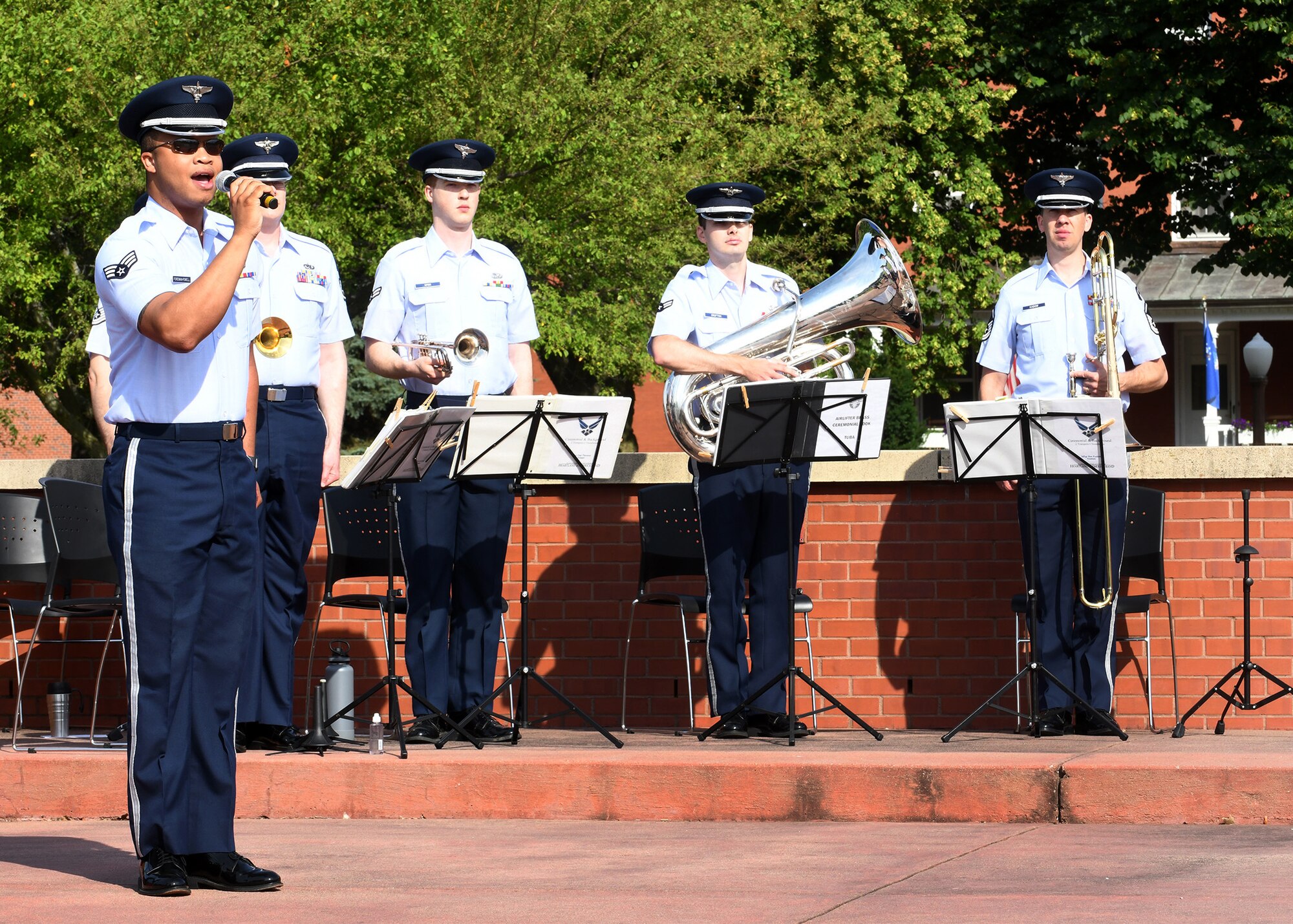 airmen in uniform in the background holding different musical instruments and in the forefront airman holding a microphone and singing