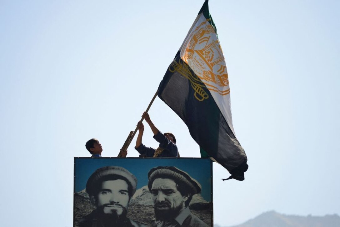 Afghan men wave a flag above the portrait of late Afghan commander Ahmad Shah Massoud
