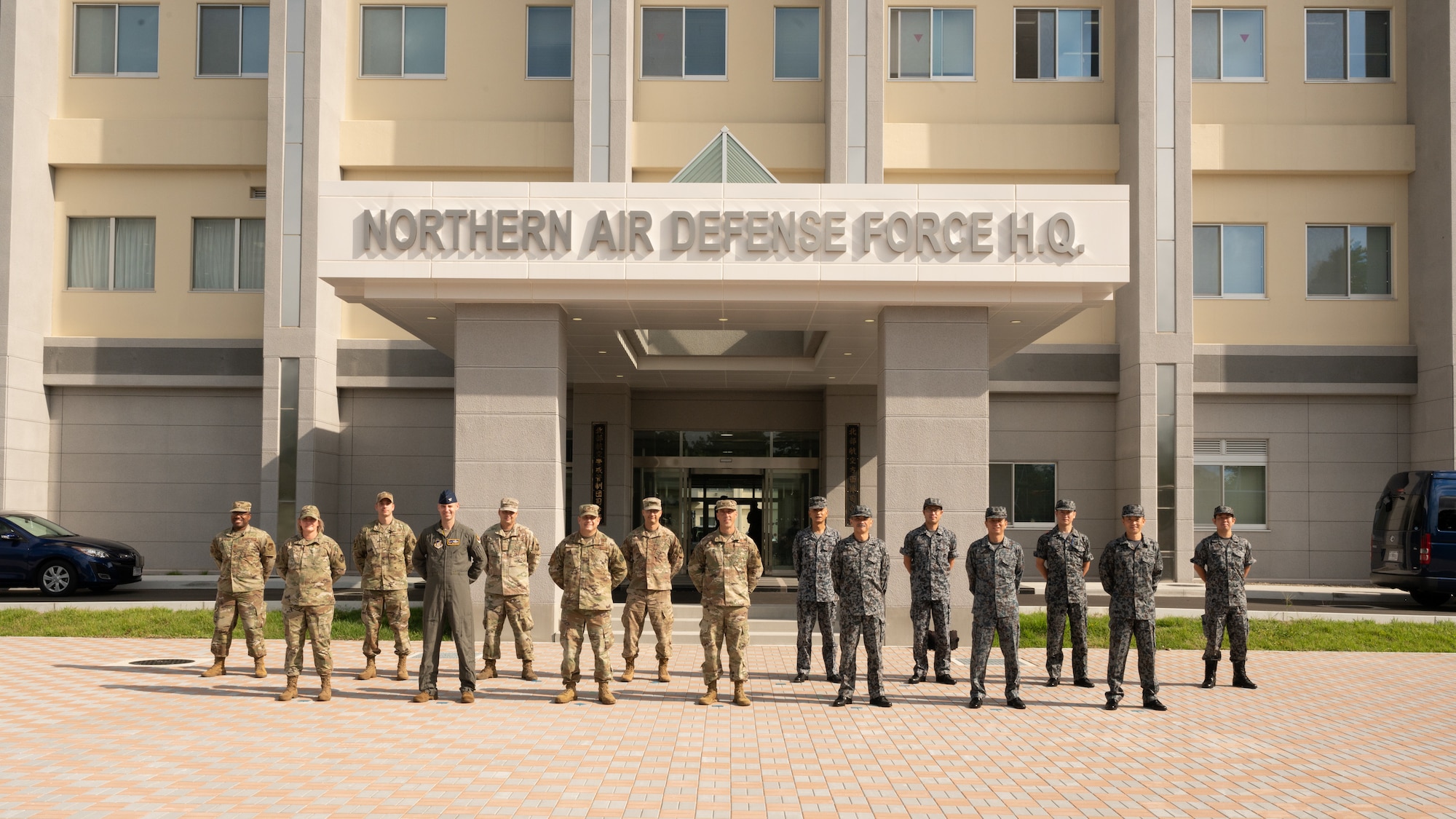 Several uniformed people stand in formation in front of a building that reads: Northern Air Defense Force H.Q.